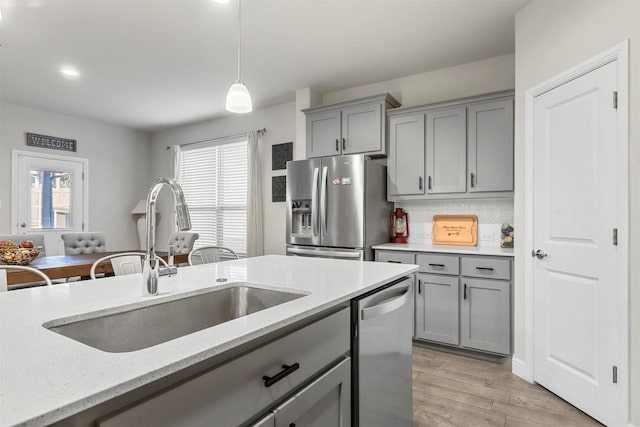 kitchen with gray cabinetry, a sink, light wood-style floors, appliances with stainless steel finishes, and light stone countertops