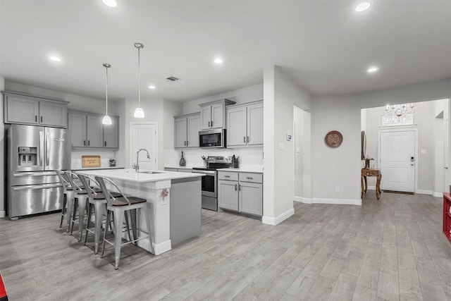 kitchen featuring a breakfast bar, gray cabinets, a sink, appliances with stainless steel finishes, and light countertops