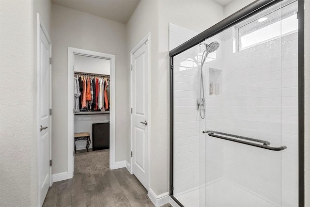 bathroom with a walk in closet, wood finished floors, a stall shower, and baseboards