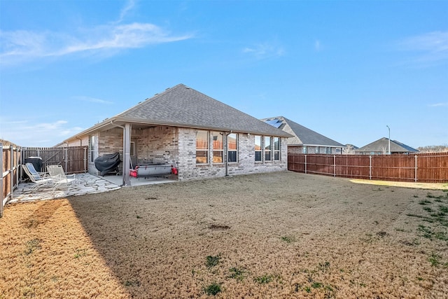 rear view of house with a patio, a fenced backyard, brick siding, and roof with shingles