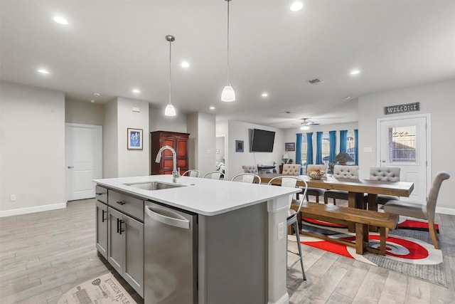 kitchen with a sink, light wood-type flooring, stainless steel dishwasher, and a kitchen island with sink