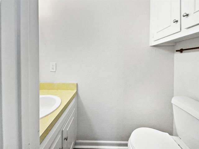 half bath featuring vanity, toilet, and baseboards