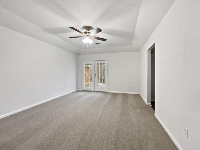 empty room with a ceiling fan, a tray ceiling, french doors, carpet floors, and baseboards