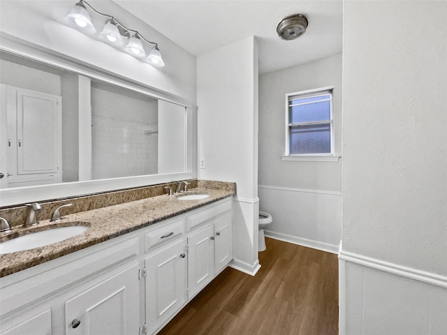 full bathroom with a sink, toilet, wood finished floors, and double vanity