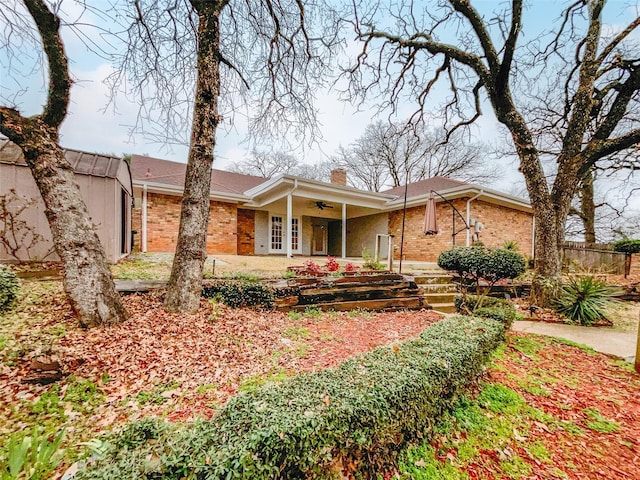 view of front of home with brick siding, ceiling fan, a chimney, and fence