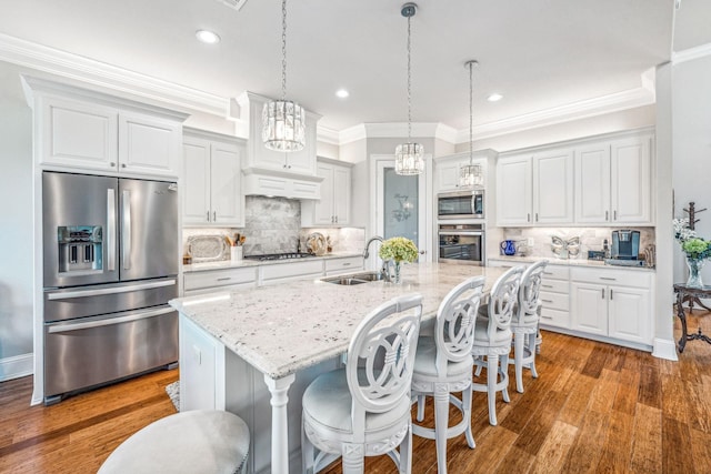 kitchen featuring ornamental molding, appliances with stainless steel finishes, an island with sink, and a sink