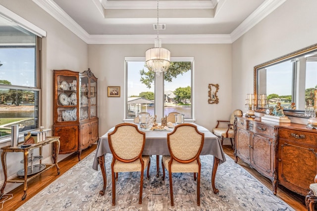 dining space with a raised ceiling, light wood-style flooring, crown molding, and a chandelier