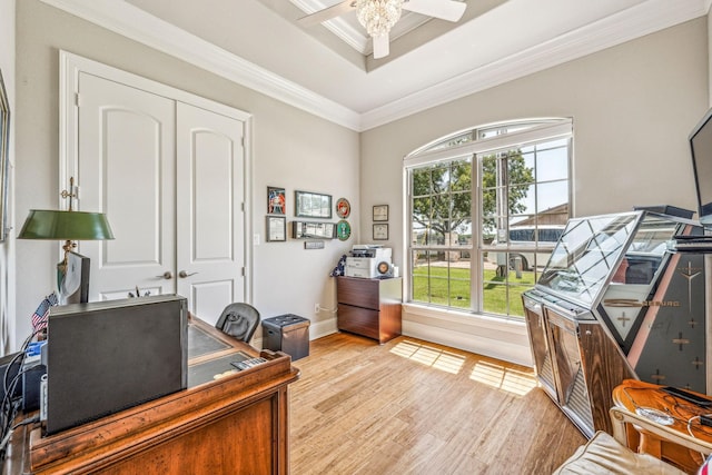 home office with a ceiling fan, baseboards, light wood-style flooring, ornamental molding, and a raised ceiling