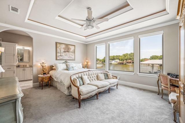 bedroom featuring arched walkways, light colored carpet, a raised ceiling, and baseboards