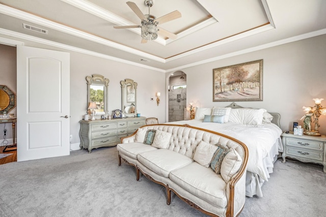 bedroom with a tray ceiling, light colored carpet, arched walkways, and ornamental molding