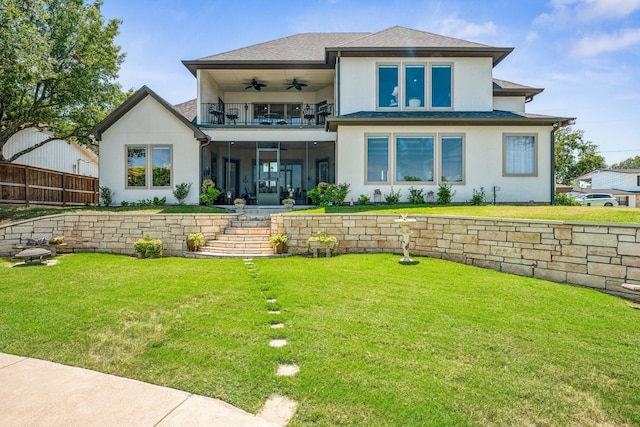 rear view of property featuring stucco siding, a lawn, a ceiling fan, fence, and a balcony