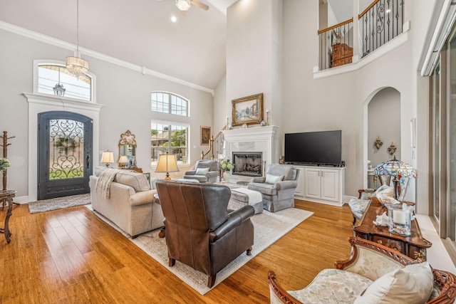 living room featuring baseboards, light wood finished floors, a high ceiling, a fireplace, and arched walkways