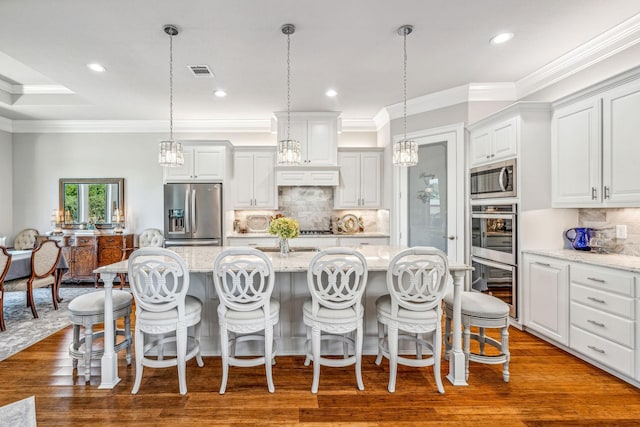 kitchen featuring a center island with sink, visible vents, appliances with stainless steel finishes, pendant lighting, and crown molding