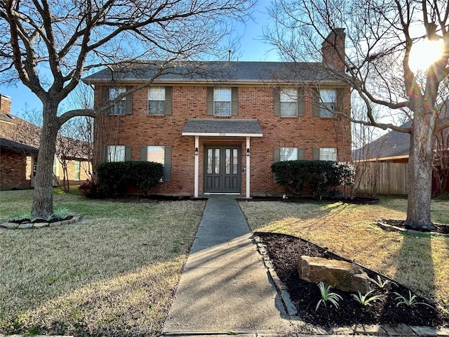 colonial-style house with brick siding, a front lawn, fence, french doors, and a chimney