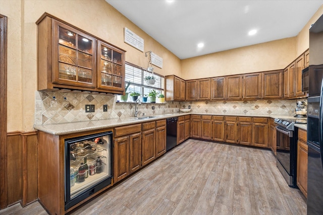 kitchen featuring light countertops, light wood-style flooring, brown cabinets, black appliances, and a sink