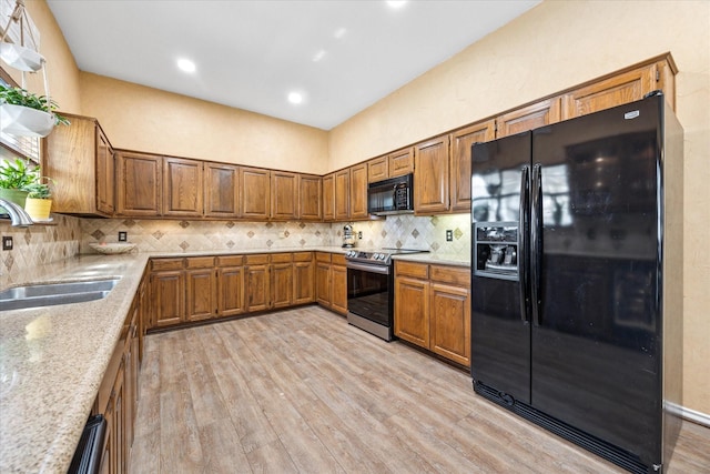 kitchen with tasteful backsplash, light wood-style flooring, brown cabinetry, black appliances, and a sink