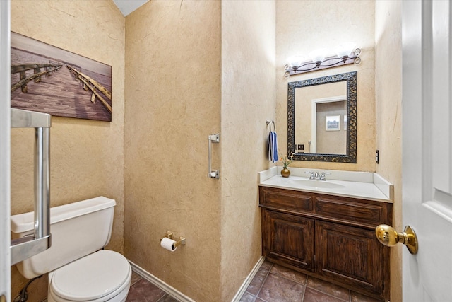 bathroom featuring tile patterned flooring, baseboards, toilet, a textured wall, and vanity