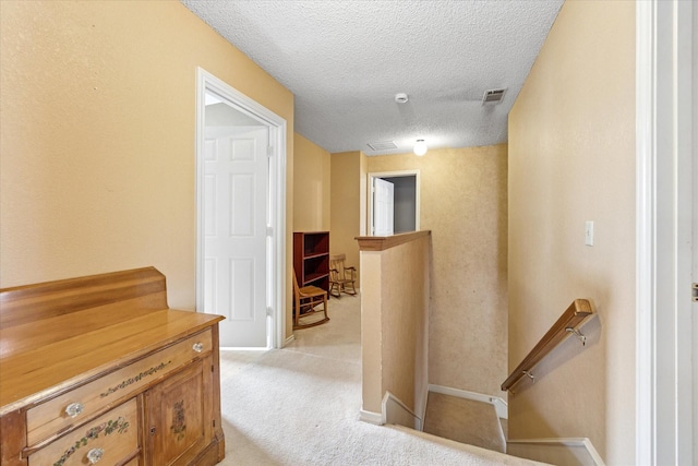 hallway featuring baseboards, visible vents, an upstairs landing, a textured ceiling, and light colored carpet