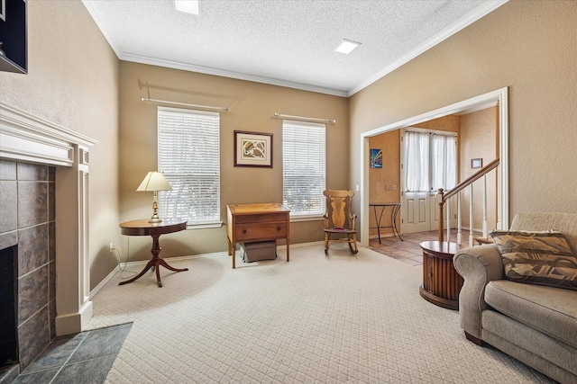 sitting room with a tiled fireplace, a textured ceiling, crown molding, and carpet