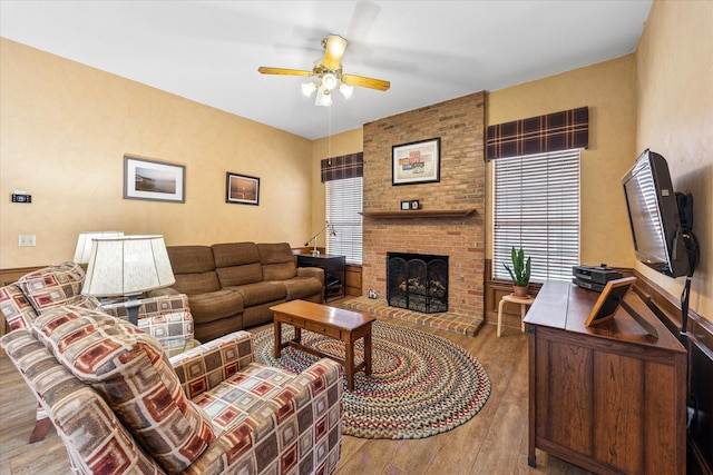 living room featuring a brick fireplace, a ceiling fan, and wood finished floors