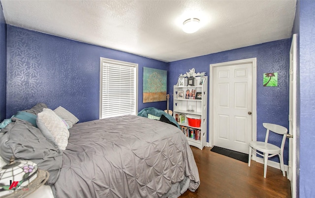 bedroom with baseboards, a textured ceiling, wood finished floors, and a textured wall