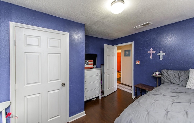 bedroom with visible vents, a textured ceiling, wood finished floors, baseboards, and a textured wall