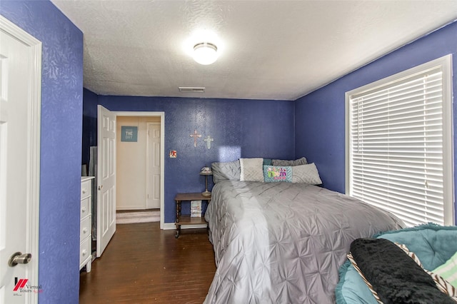 bedroom featuring visible vents, baseboards, wood finished floors, a textured wall, and a textured ceiling