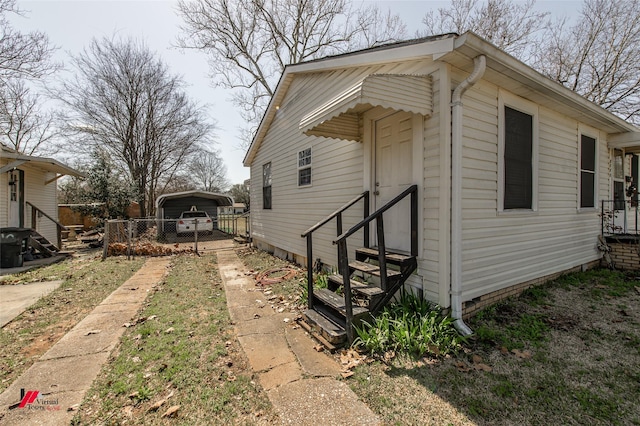 view of property exterior featuring a detached carport, entry steps, driveway, and fence