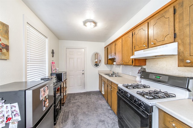 kitchen featuring brown cabinetry, light countertops, gas range oven, under cabinet range hood, and dark colored carpet