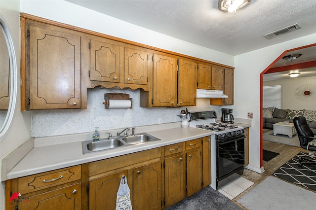 kitchen with visible vents, a sink, under cabinet range hood, gas range oven, and brown cabinetry