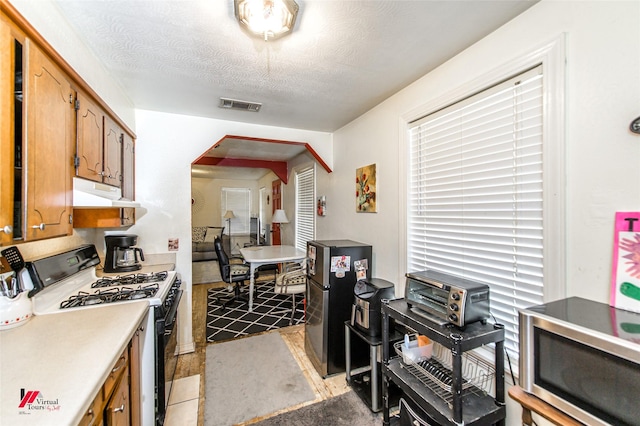 kitchen featuring visible vents, under cabinet range hood, gas range oven, arched walkways, and light countertops