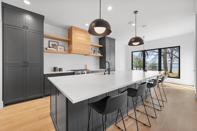 kitchen with visible vents, an island with sink, open shelves, light wood-style floors, and light countertops