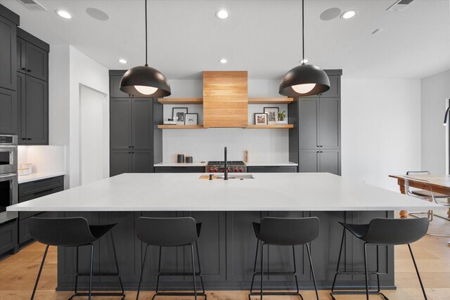 kitchen with a sink, light countertops, light wood-style floors, and open shelves