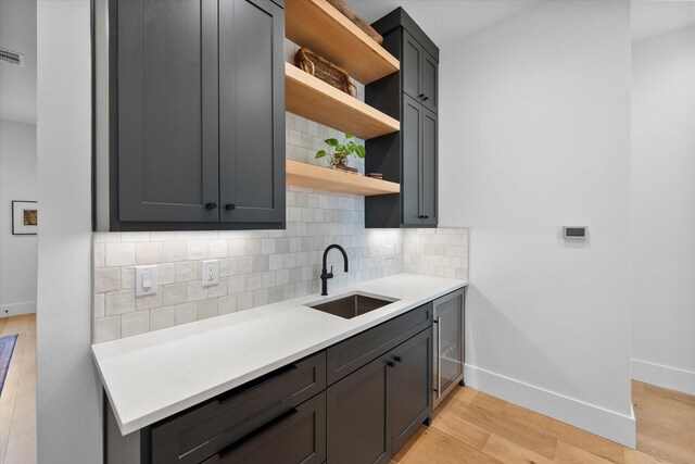 kitchen with light wood finished floors, a sink, open shelves, light countertops, and decorative backsplash