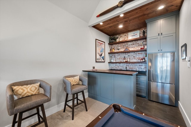 bar with baseboards, recessed lighting, indoor wet bar, vaulted ceiling, and built in fridge