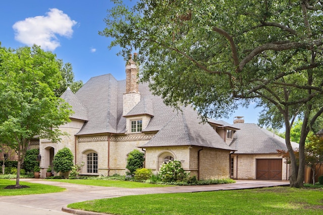 french provincial home with stone siding, a chimney, concrete driveway, a front yard, and a garage