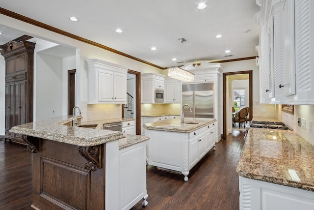 kitchen with built in appliances, a sink, a peninsula, recessed lighting, and an island with sink