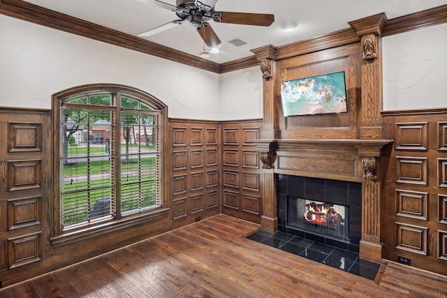unfurnished living room featuring ornamental molding, a ceiling fan, a fireplace, dark wood finished floors, and a wainscoted wall