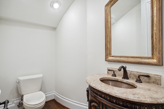 bathroom with toilet, vaulted ceiling, vanity, baseboards, and wood finished floors
