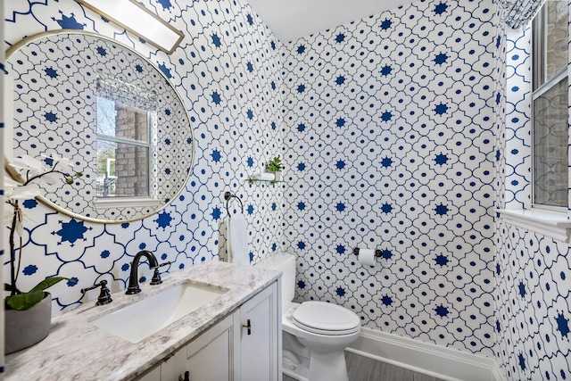 bathroom featuring toilet, vanity, and wallpapered walls