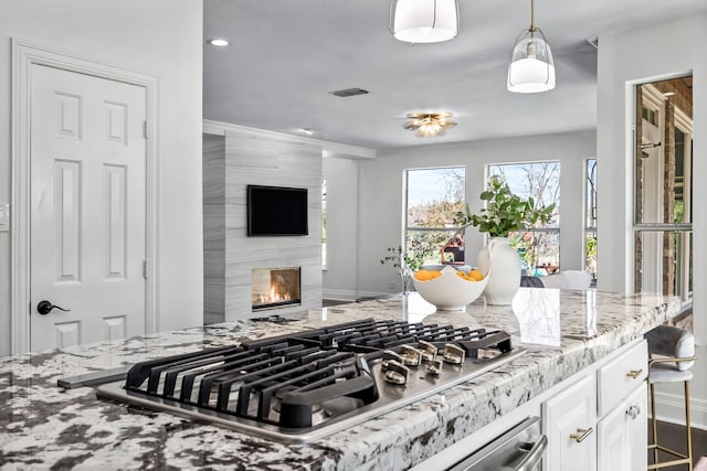 kitchen featuring light stone countertops, visible vents, stainless steel gas cooktop, a fireplace, and white cabinets