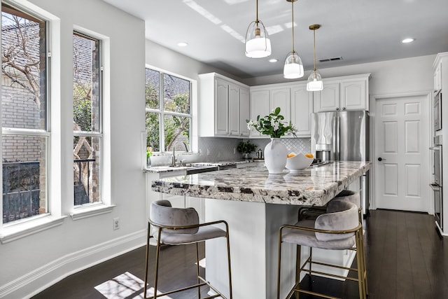 kitchen with a kitchen bar, light stone countertops, decorative backsplash, and stainless steel refrigerator with ice dispenser