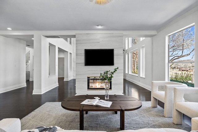 living room with crown molding, wood finished floors, baseboards, and a large fireplace