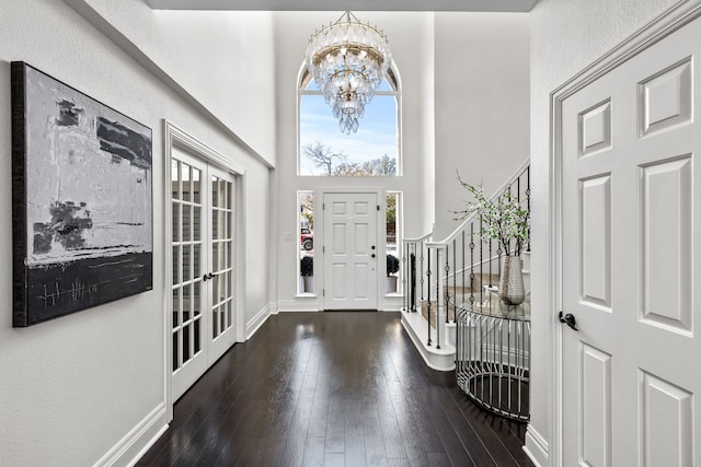 entryway featuring baseboards, stairs, hardwood / wood-style floors, a towering ceiling, and an inviting chandelier