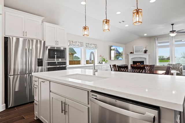 kitchen with a sink, a warm lit fireplace, open floor plan, dark wood-style floors, and stainless steel appliances