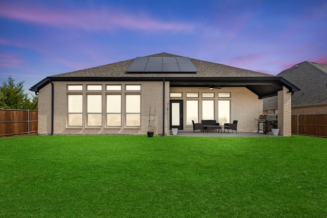 back of property at dusk featuring solar panels, a patio area, brick siding, and a fenced backyard