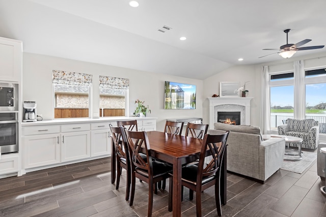 dining room with wood finish floors, recessed lighting, ceiling fan, vaulted ceiling, and a glass covered fireplace