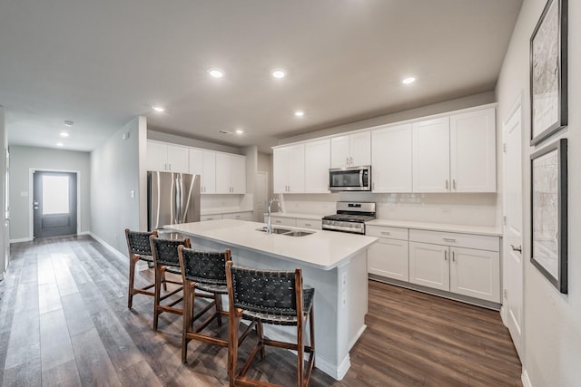 kitchen featuring dark wood-type flooring, a center island with sink, white cabinets, stainless steel appliances, and a sink