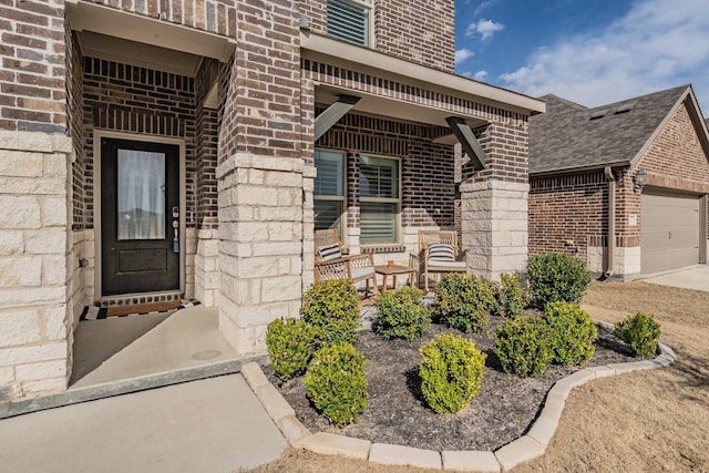 doorway to property with brick siding, a porch, concrete driveway, and a garage