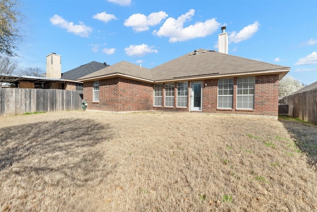 rear view of house featuring brick siding, a lawn, a chimney, and fence